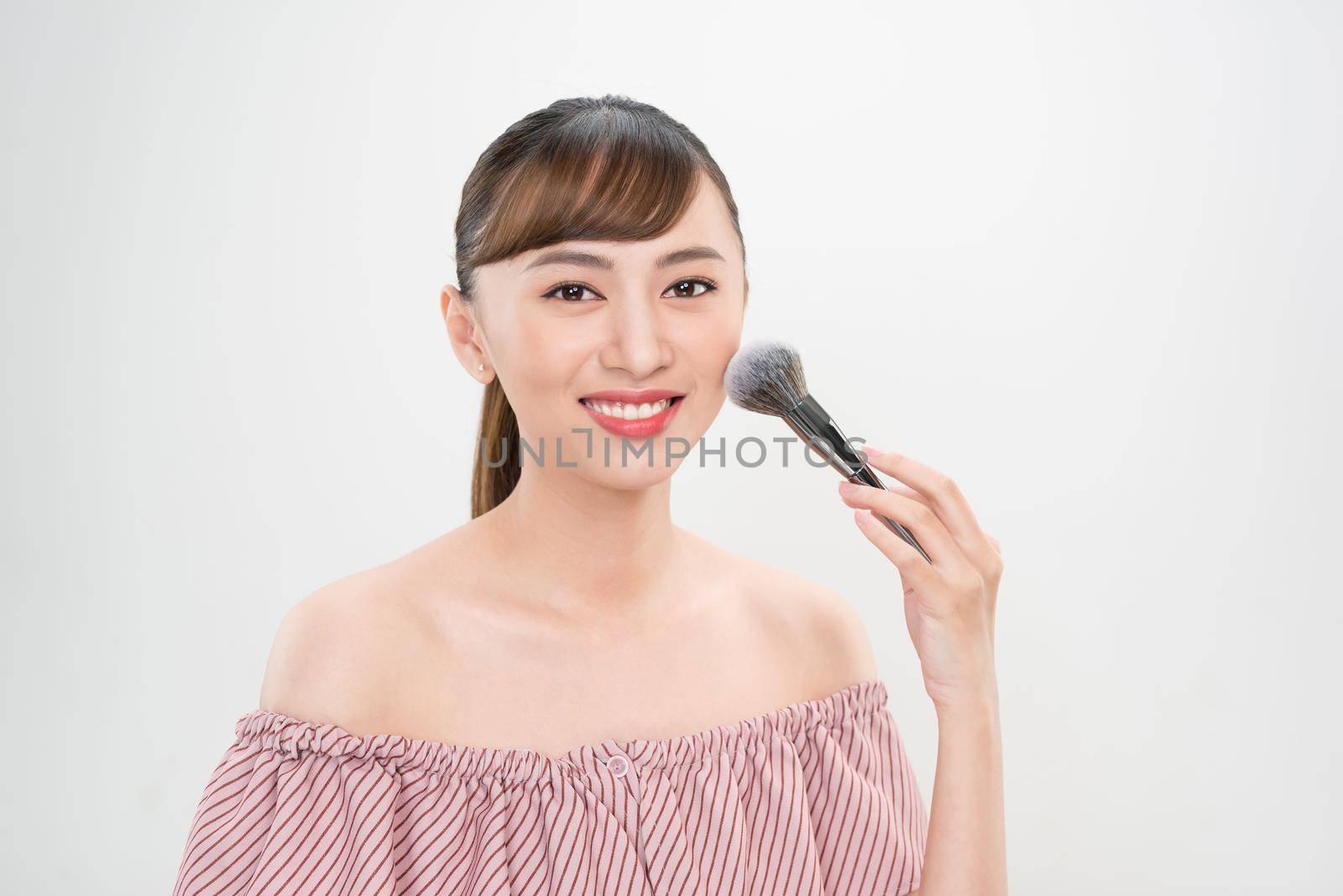 Beautiful smiling girl applying loose blush with cosmetic brush. by makidotvn