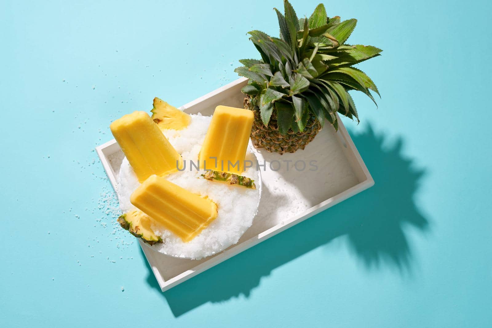 Pineapple ice pops on a tray. Top view scene over a blue background by makidotvn