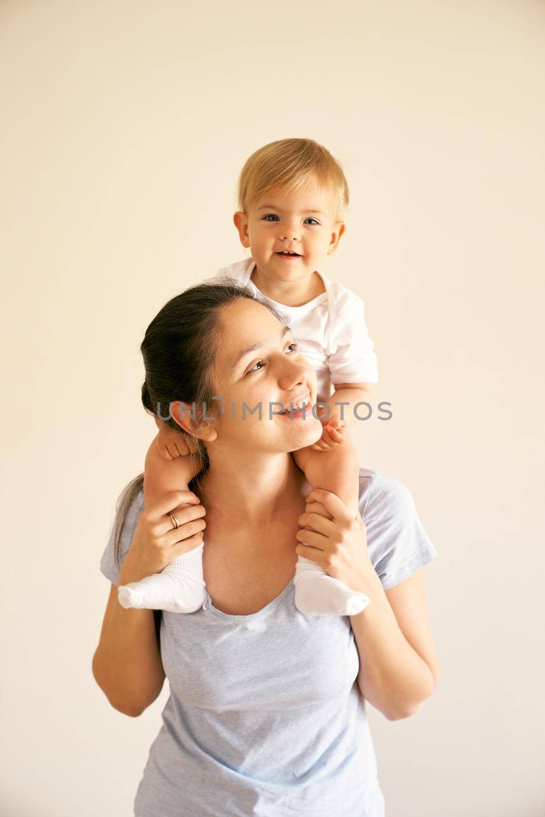 Smiling mom holds a little girl on her shoulders. Portrait by Nadtochiy