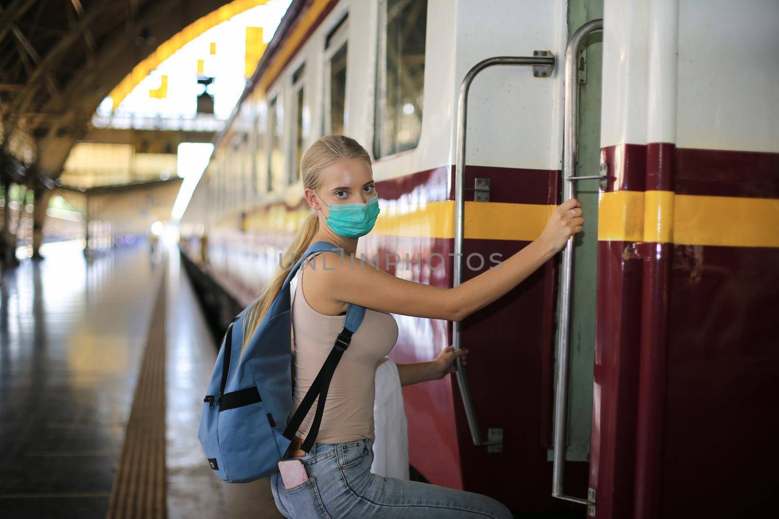young woman with face mask waiting in vintage train, relaxed and carefree at the station platform in Bangkok, Thailand before catching a train. Travel photography. Lifestyle.