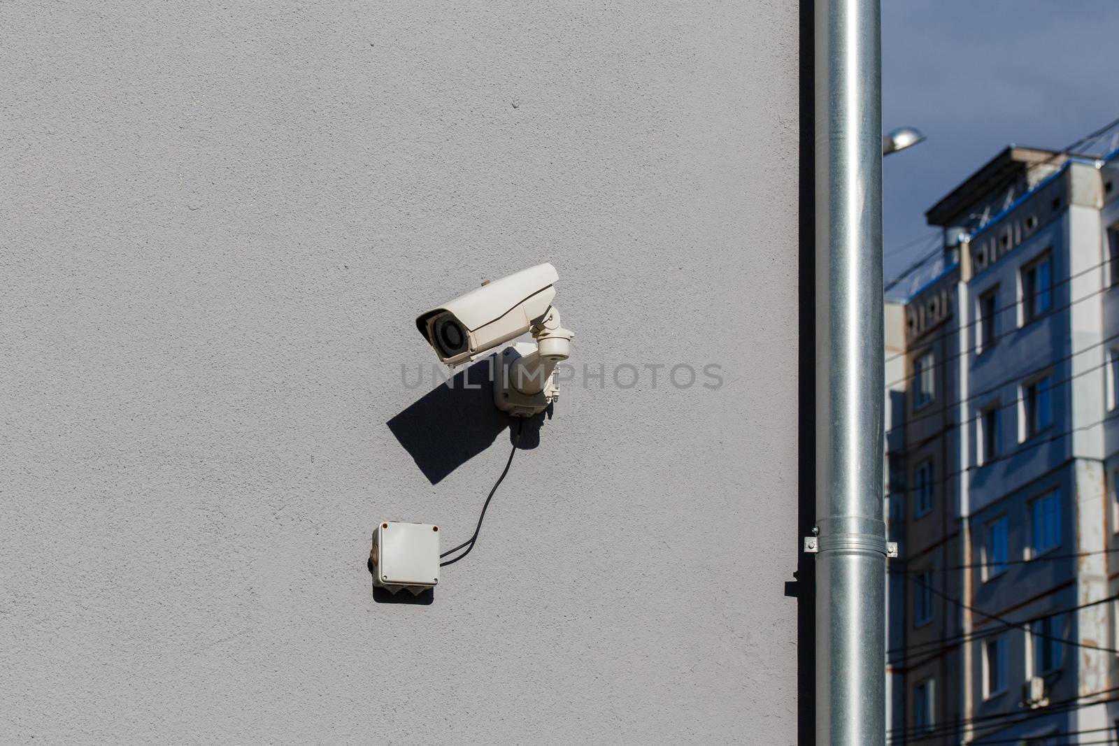 small white surveillance camera on flat gray matte plaster wall in city pointing sideways