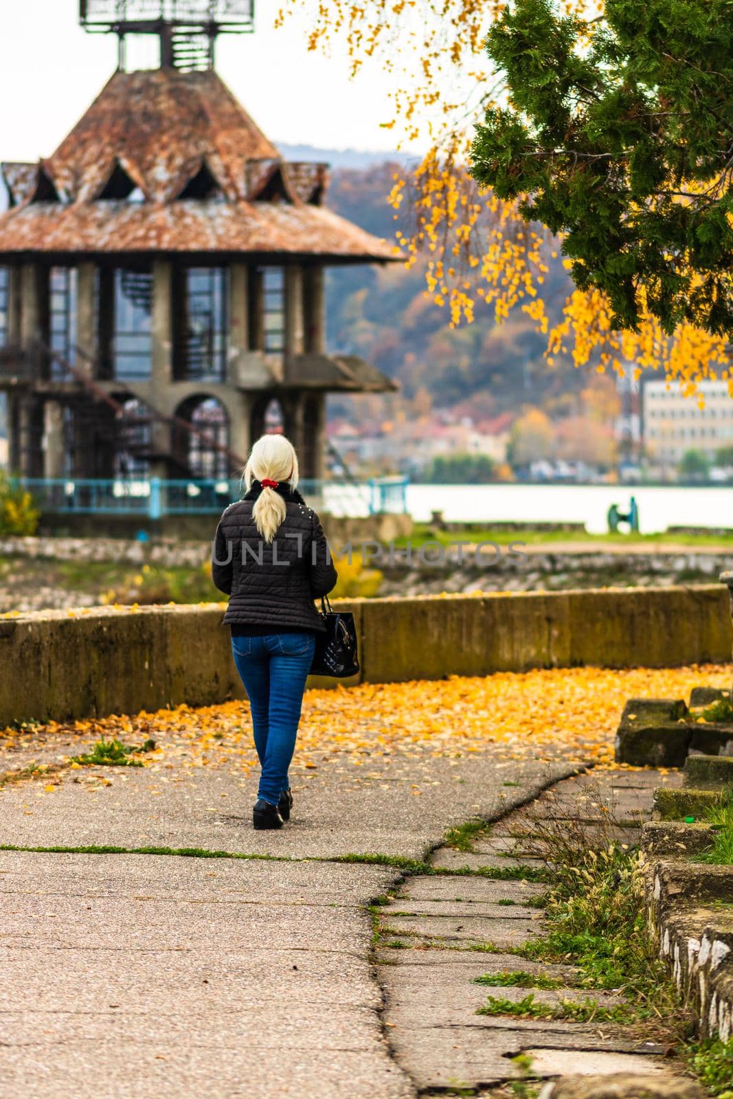 Alone woman walking on the autumn alley. Autumn landscape, orange foliage in a park in Orsova, Romania, 2020