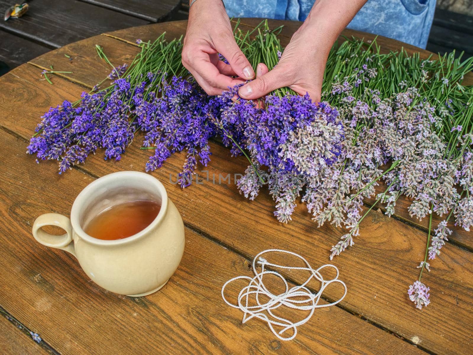 Hands of gardener woman create relaxing smell herbal bouquet. Working table with herbal tea, stalks of lavender and scissors.