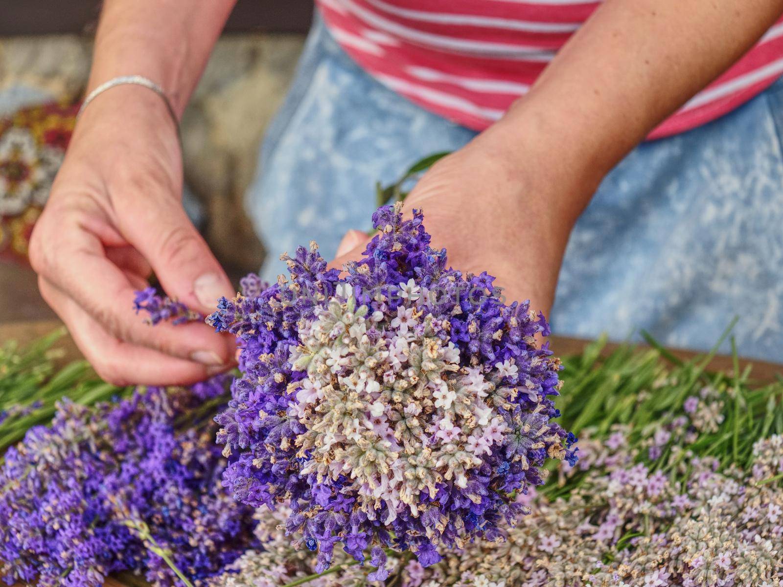 Girl hands with scissors and string preparing lavender flowers bunches on wooden table. 