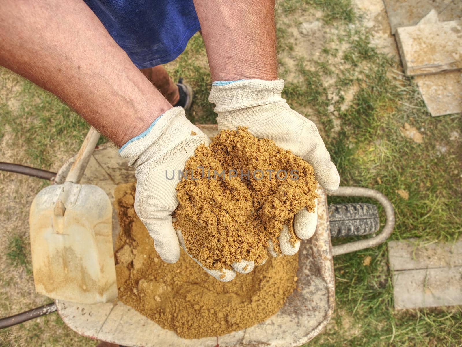 Worker hands in gloves holds sand. Wet yellow sand for building - concept of traditional construction of house. Sand on the hand.