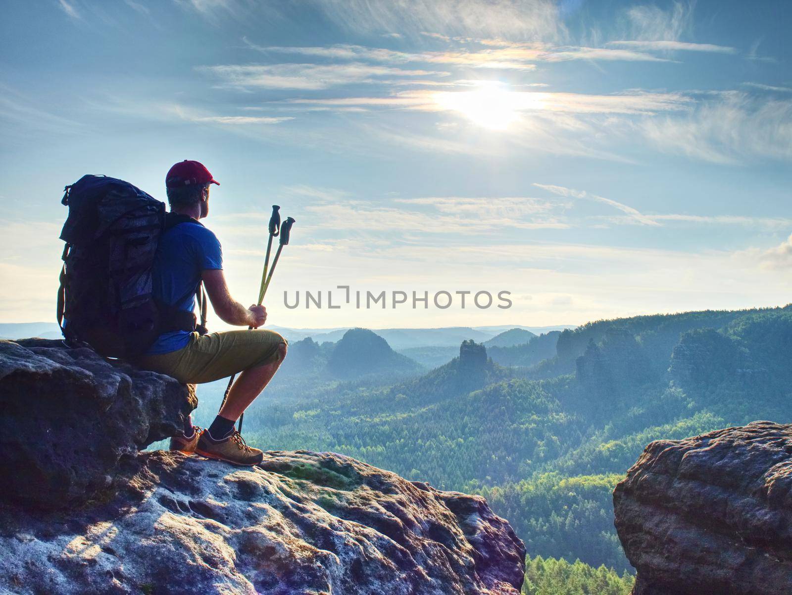 Hiker in black on the rocky peak. Daybreak in mountains, mist in deep valley. Man sit on the rock.