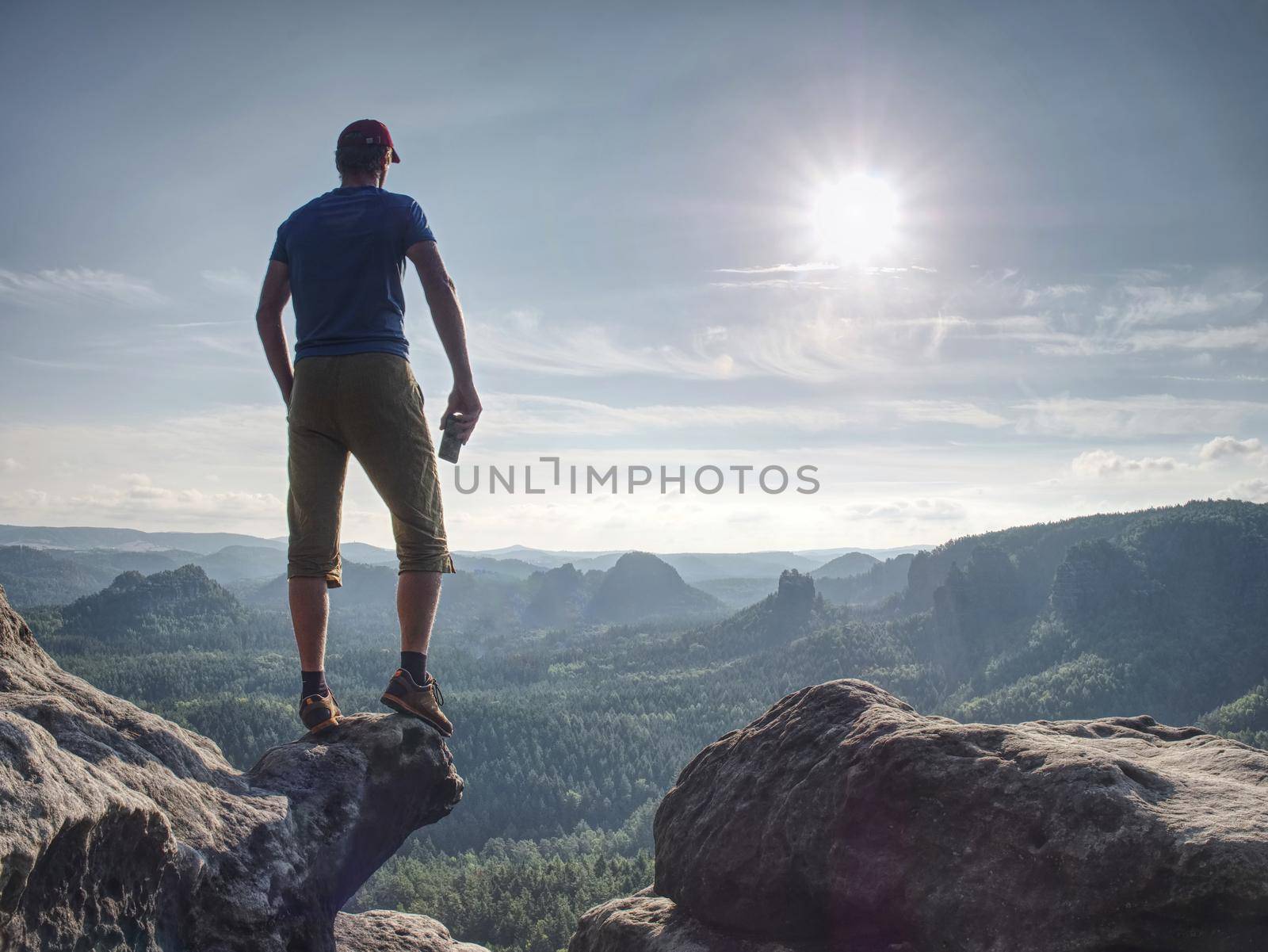 Advanture man in shorts and blue singlet watching down. Traveler on cliff mountains over  great Canyon.