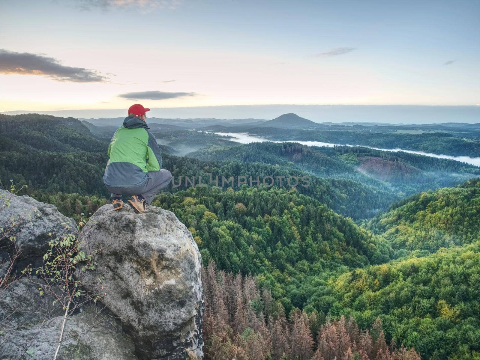 Hiker man take a rest on peak. Traveler with green windproof jacket r by rdonar2