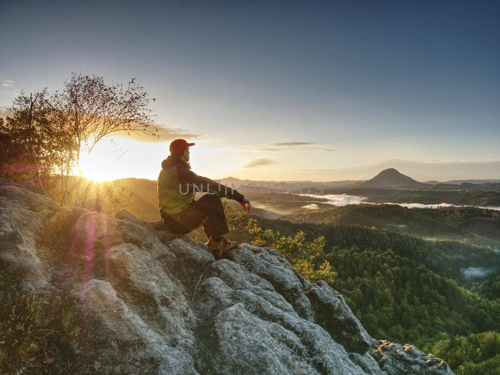 Hiker man take a rest on peak. Traveler with green windproof jacket resting on the ground and admires the mountain peaks