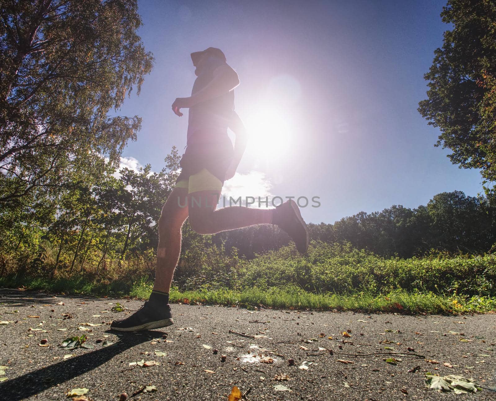 Slim body guy runs on path with fallen leaves. Warm day  by rdonar2