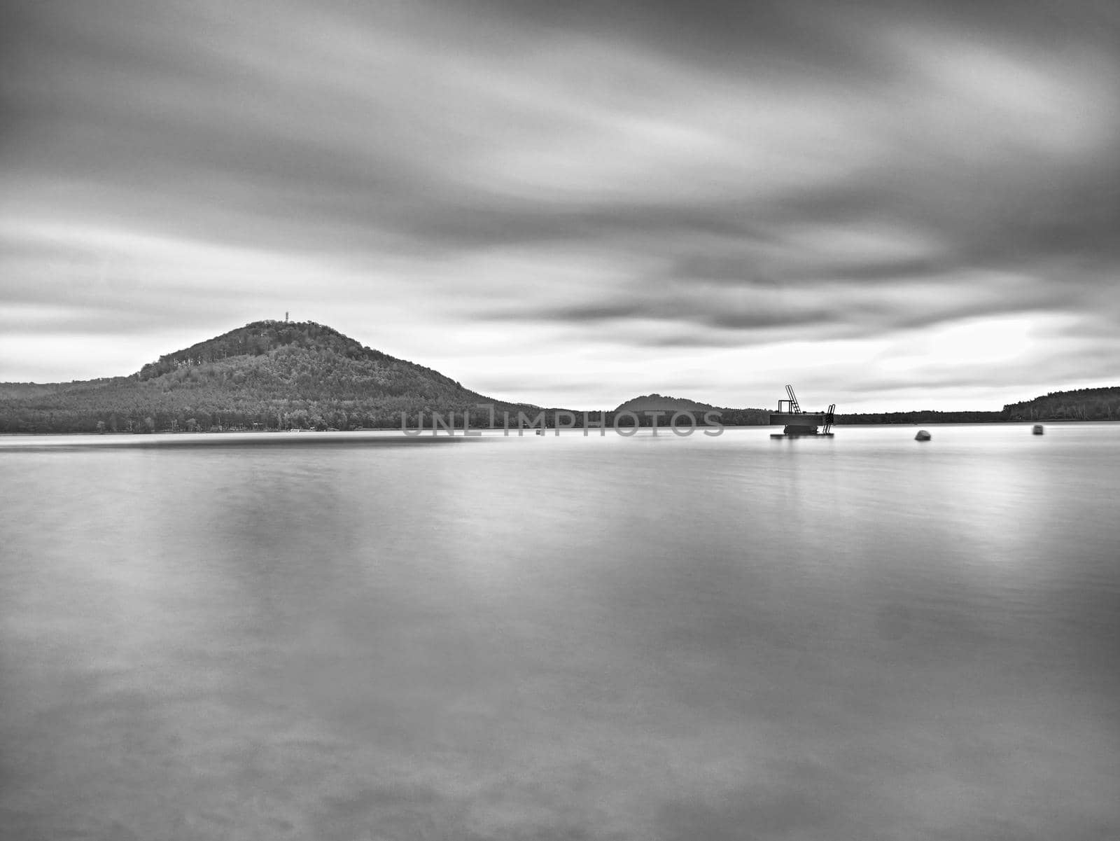 Autumn view over  low level pond to forest hill on opposite bank. Autumn melancholic atmosphere. Long exposure.   Black and white photo.