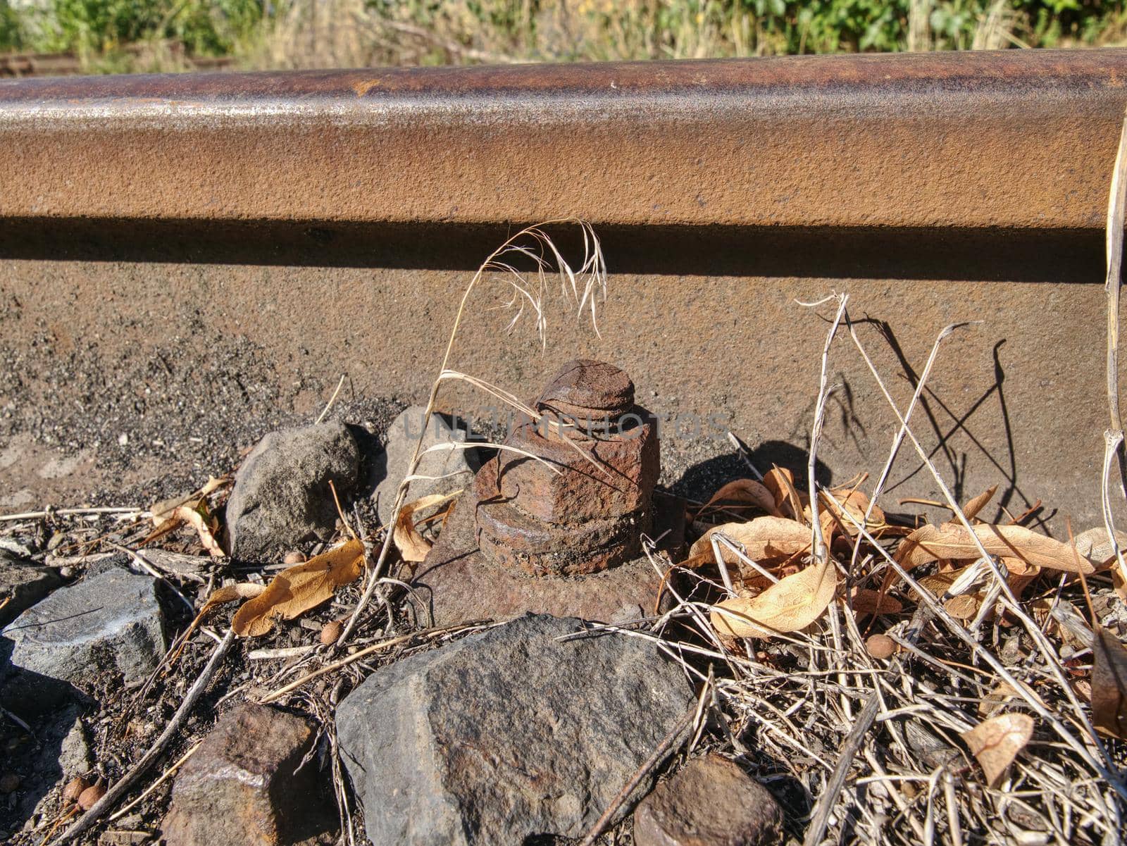 Detail of rusty screws and nut on old railroad track. Wooden oiled tie with rusty nuts and bolts. Damaged surface of rail rod. 