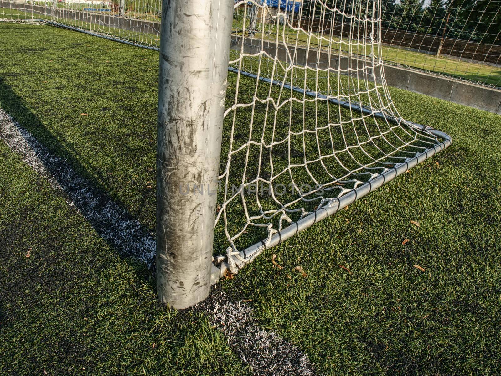 Hang bended white soccer net in  soccer football net. Grass and white painted line on football playground in the background