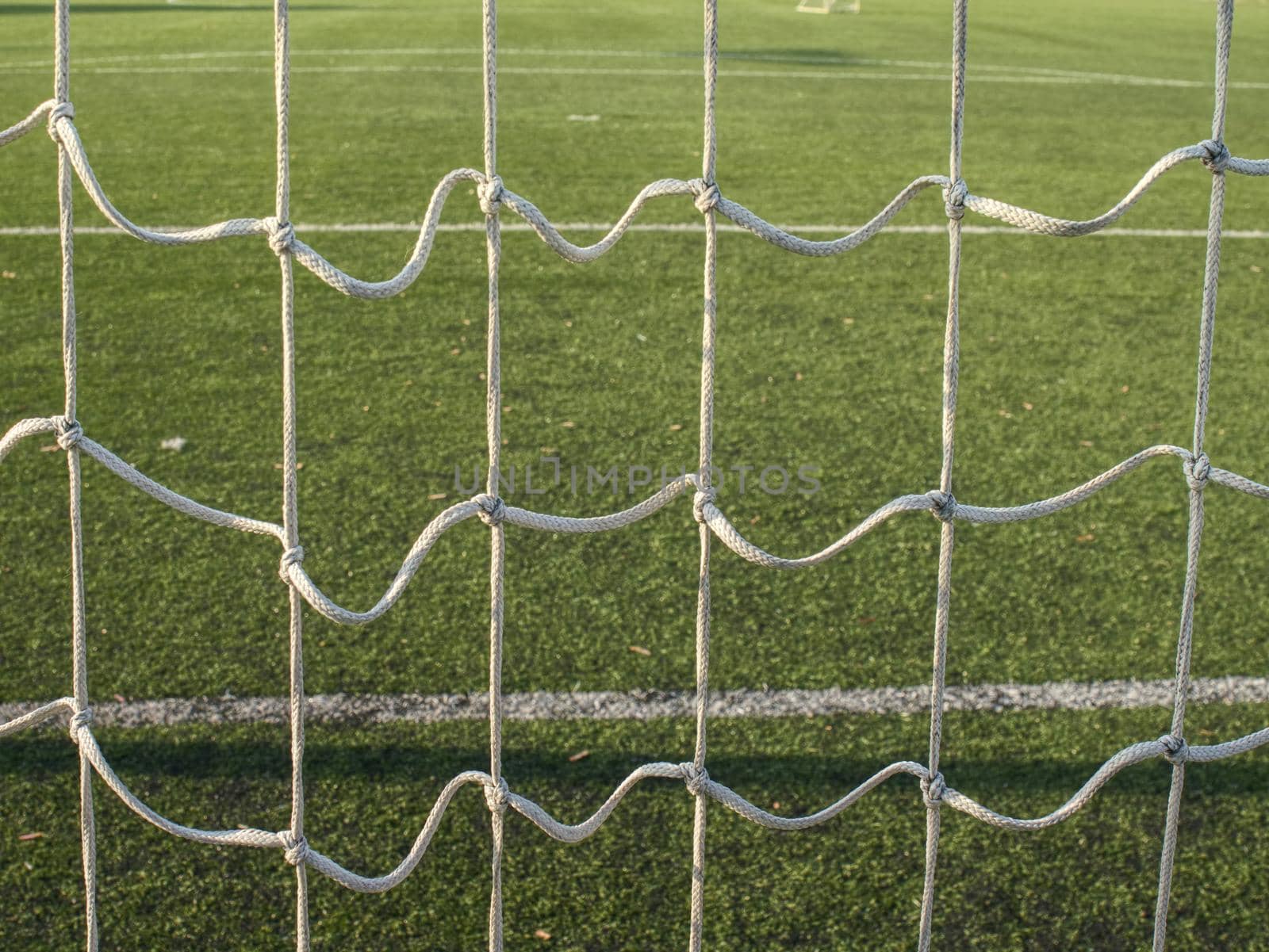 Hang bended white soccer net in  soccer football net. Grass and white painted line on football playground in the background