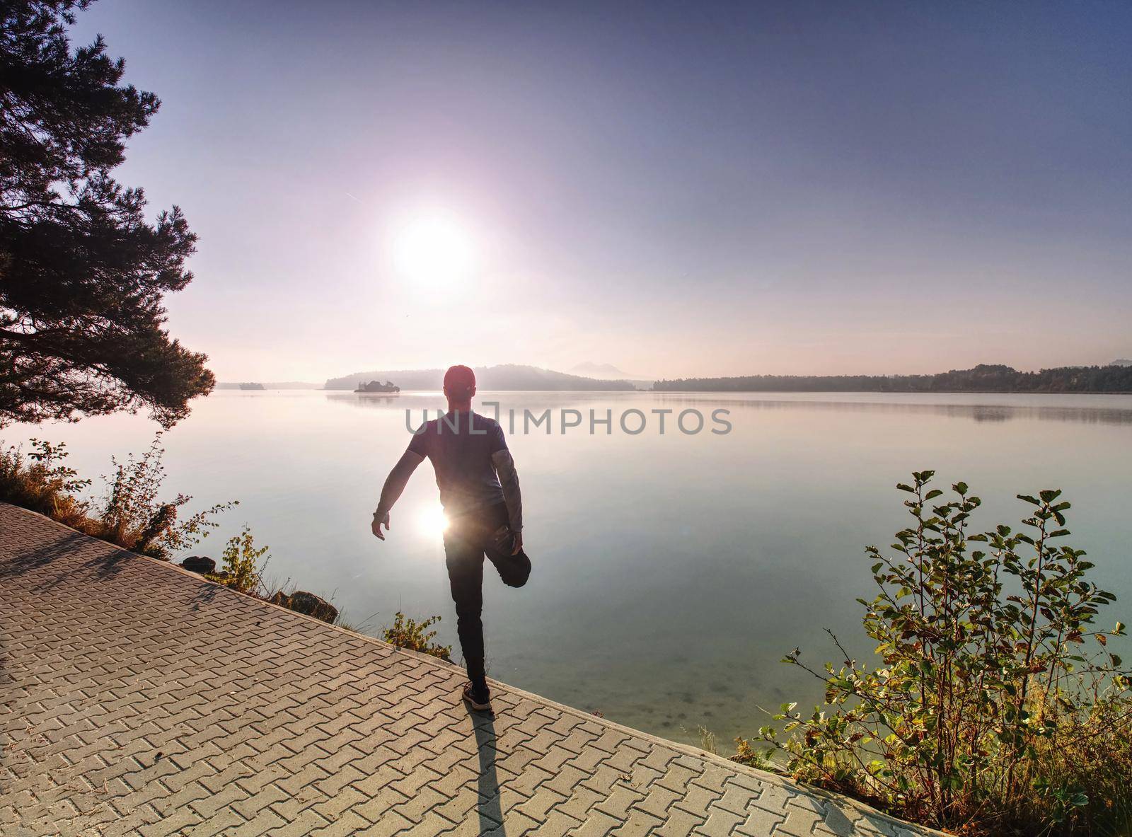 Man runner doing stretching exercise, preparing for morning workout in the lake park. Street fitness, sport, exercising, people and healthy lifestyle concept.