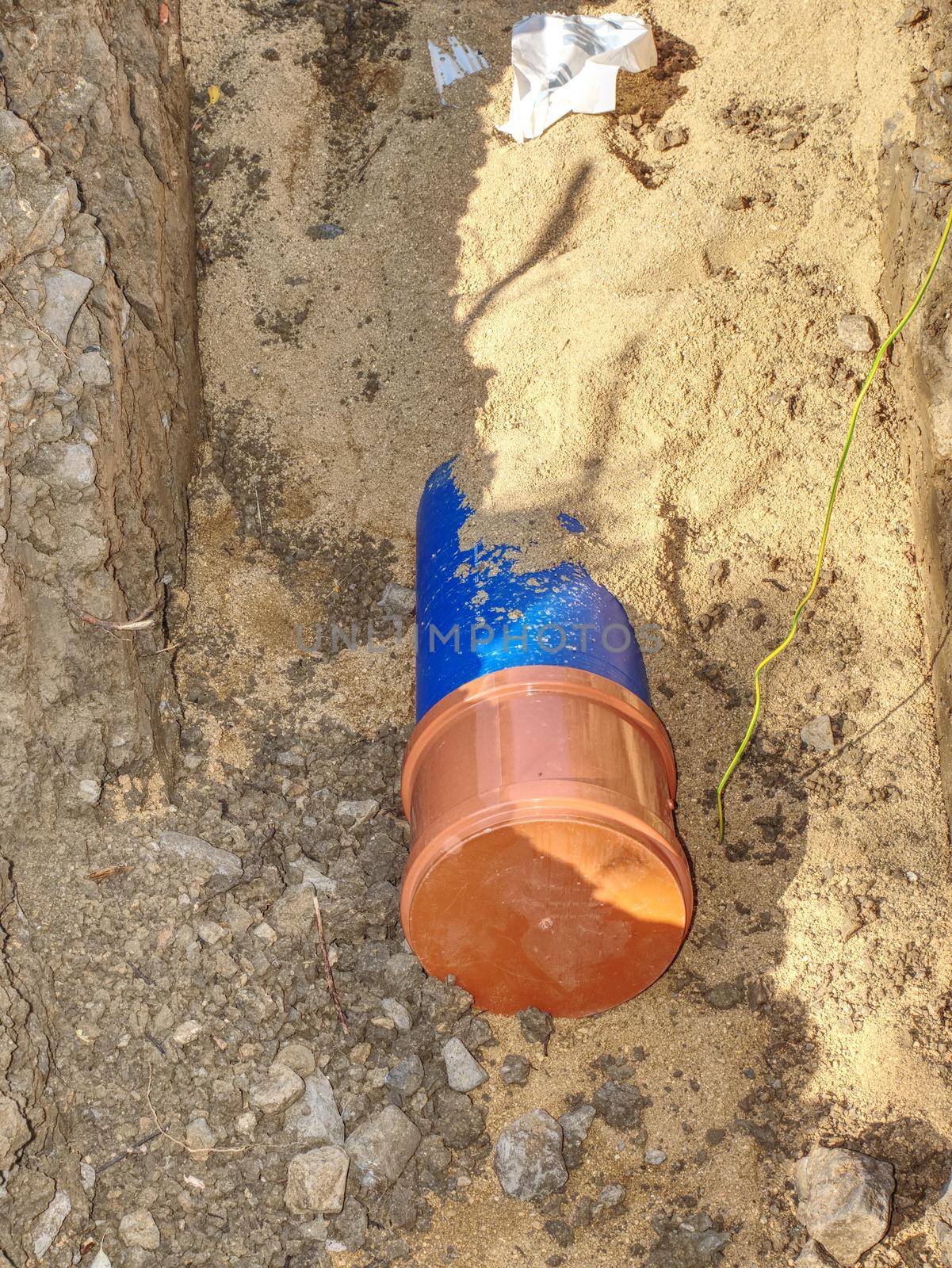 Plastic tubes in trench of sand joined together with press reduction member. Portable water supply chain in city.