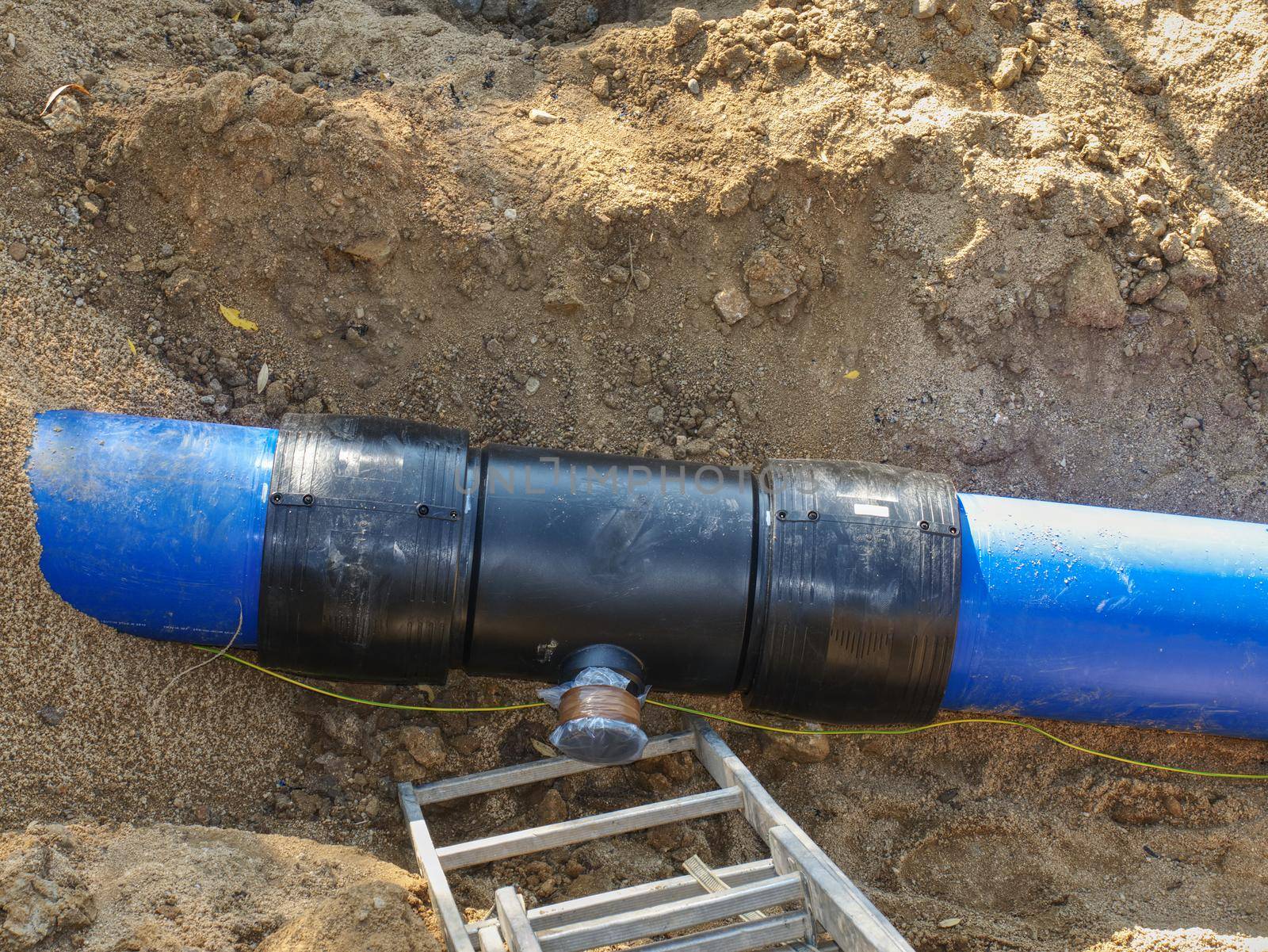 Repairing process of underground water supply pipeline. Blue plastic tubes in trench welded together with plastic pipes with joint member and screw flange.