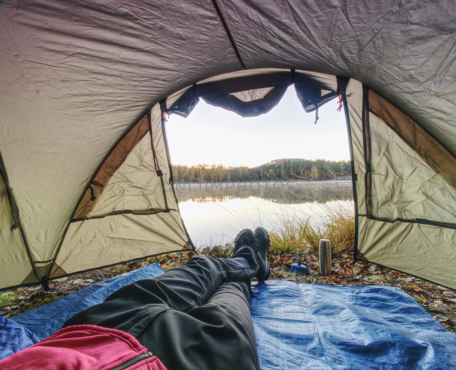 View over man body in camping tent to lake in beautiful morning. Enjoy freedom in pure nature.