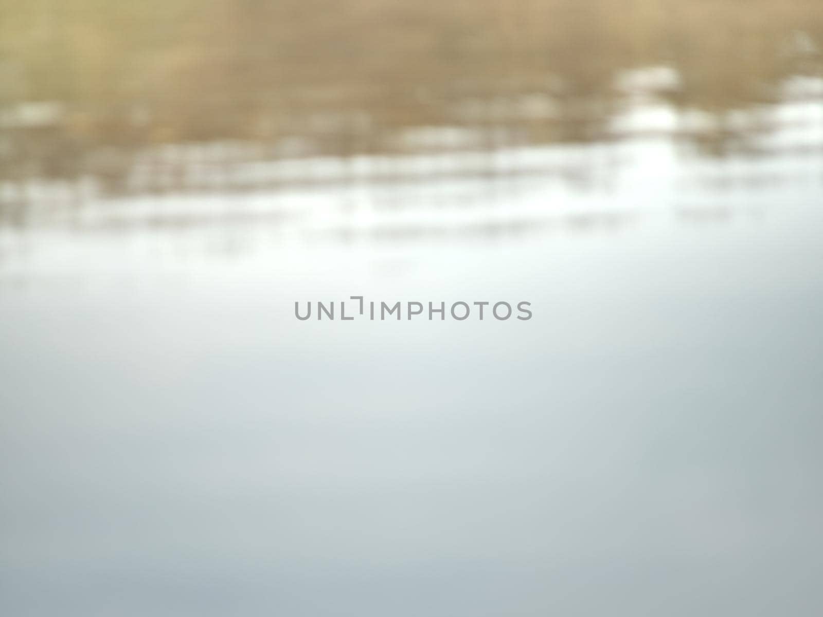 Lake water is mirroring forest on oposit bank. Romantic abstract blurry view to water level.