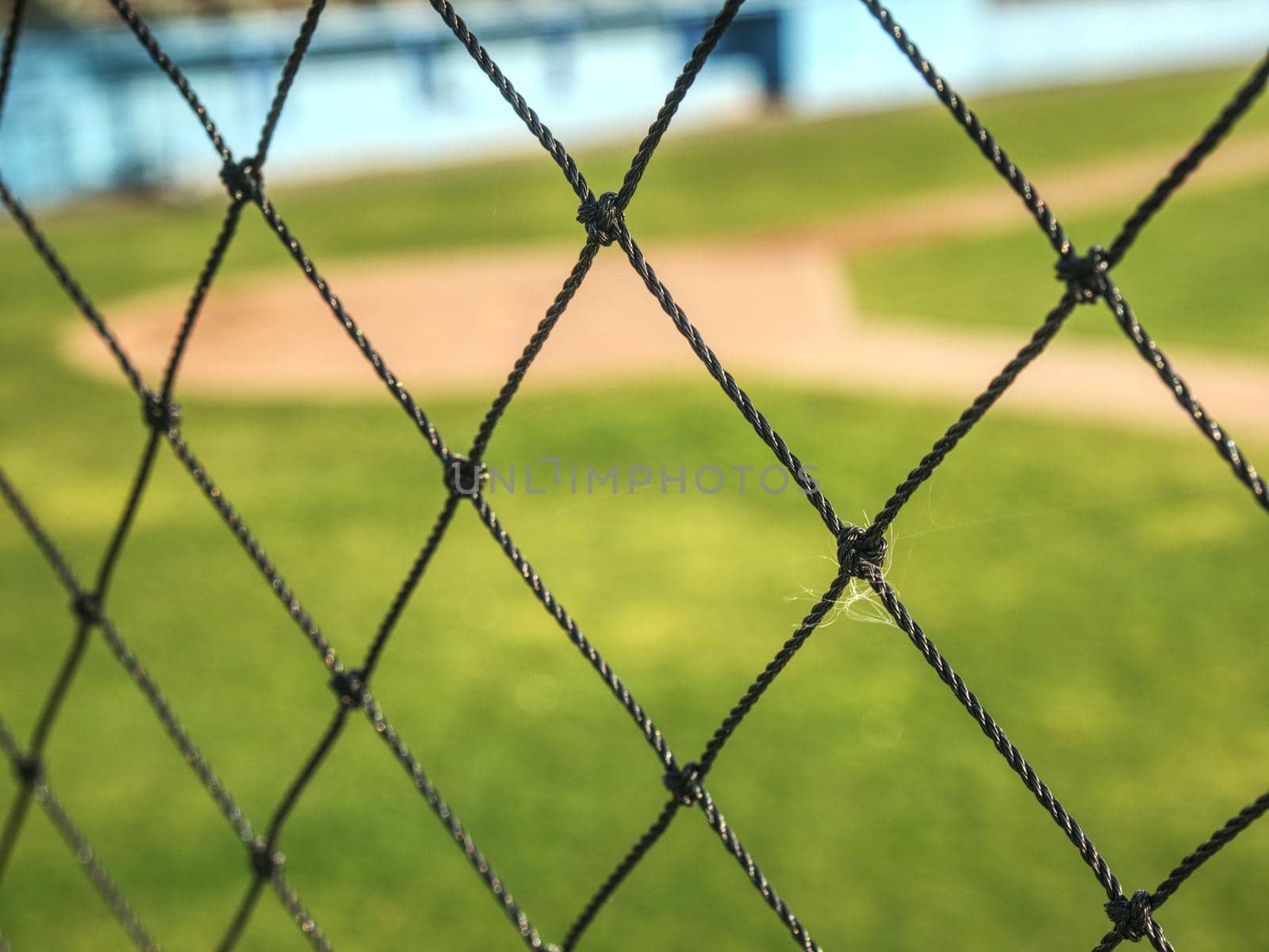 Empty baseball green field view grandstand.  View through safety net around baseball field on sunny day