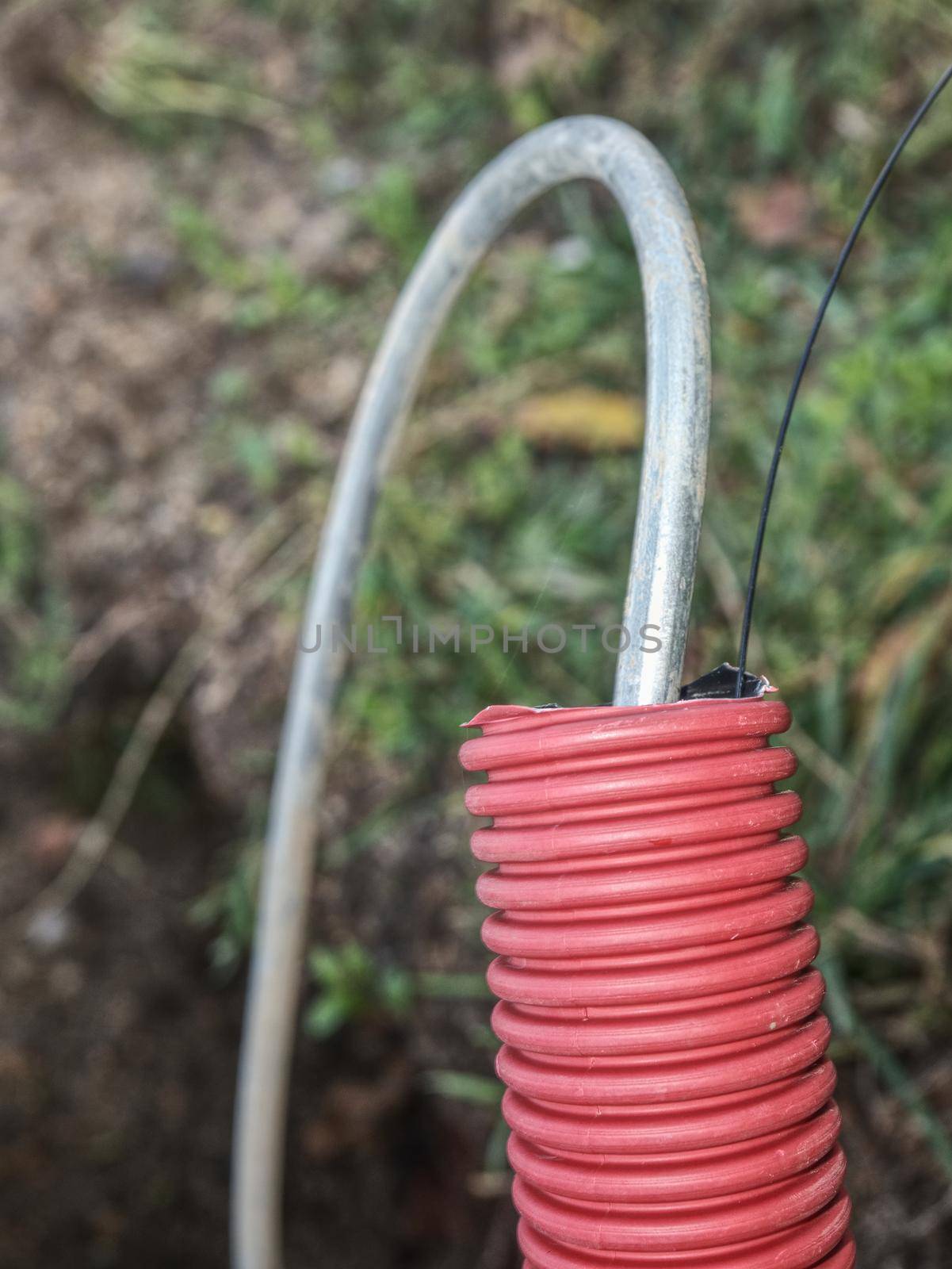 Detail of steel earthing  wire in ribbed flexible and red plastic tube, thin trench at lamp post.