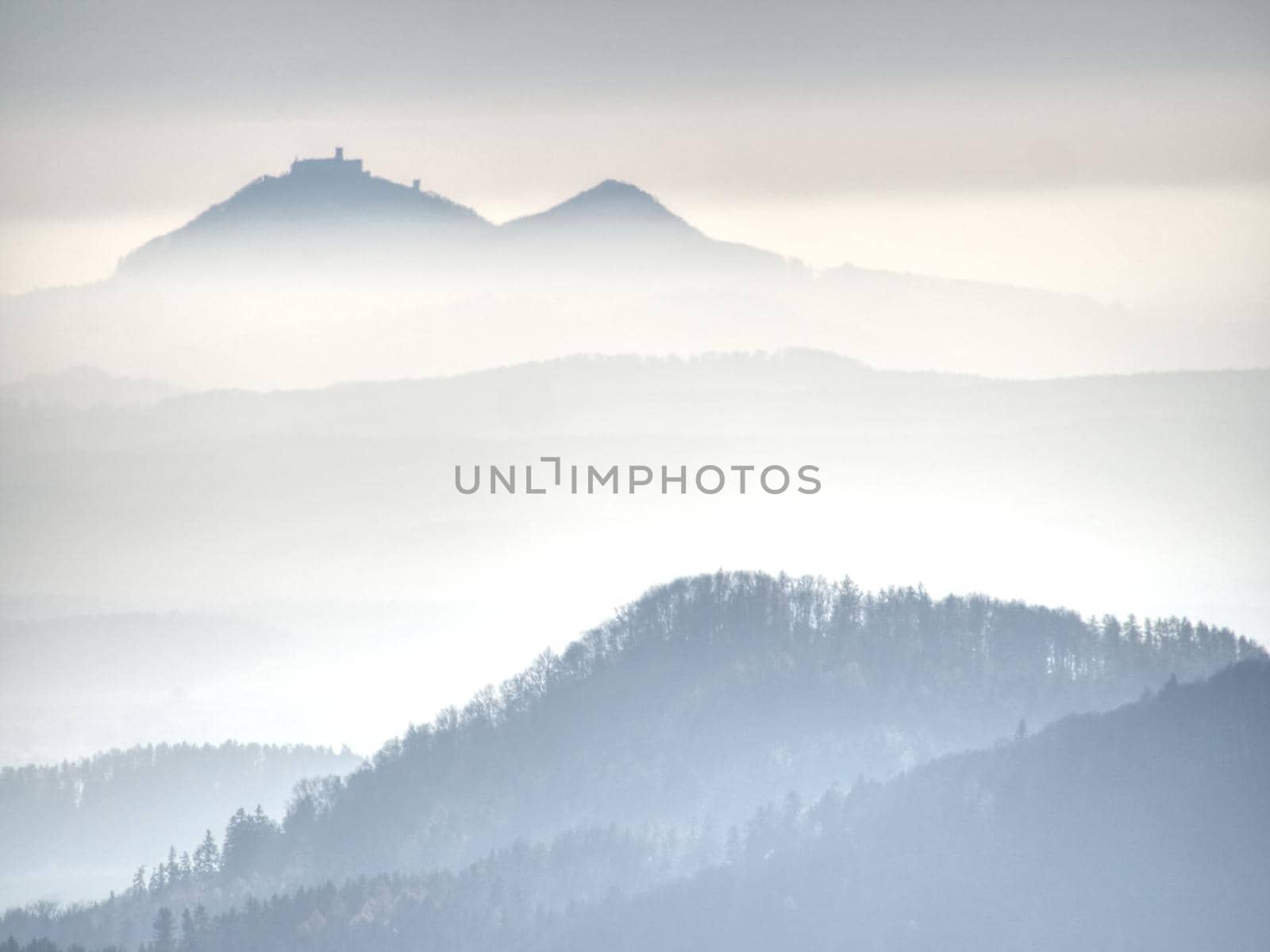 Blue mist above rounded hills in Landscape. Outline of real landscape in morning golden light.