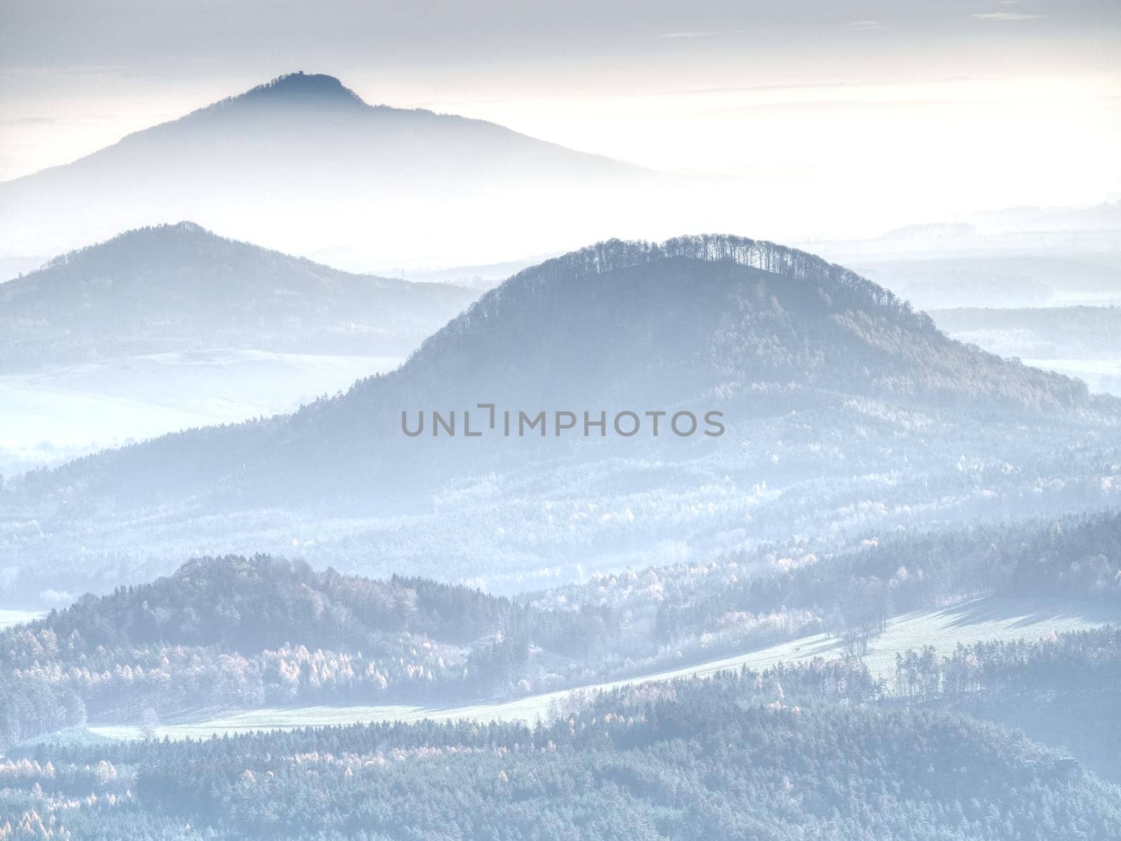 Soft outlines of hills in mist and villages in fall landscape. Unclear view to contours of hilly sides and peaks. Soft focus.