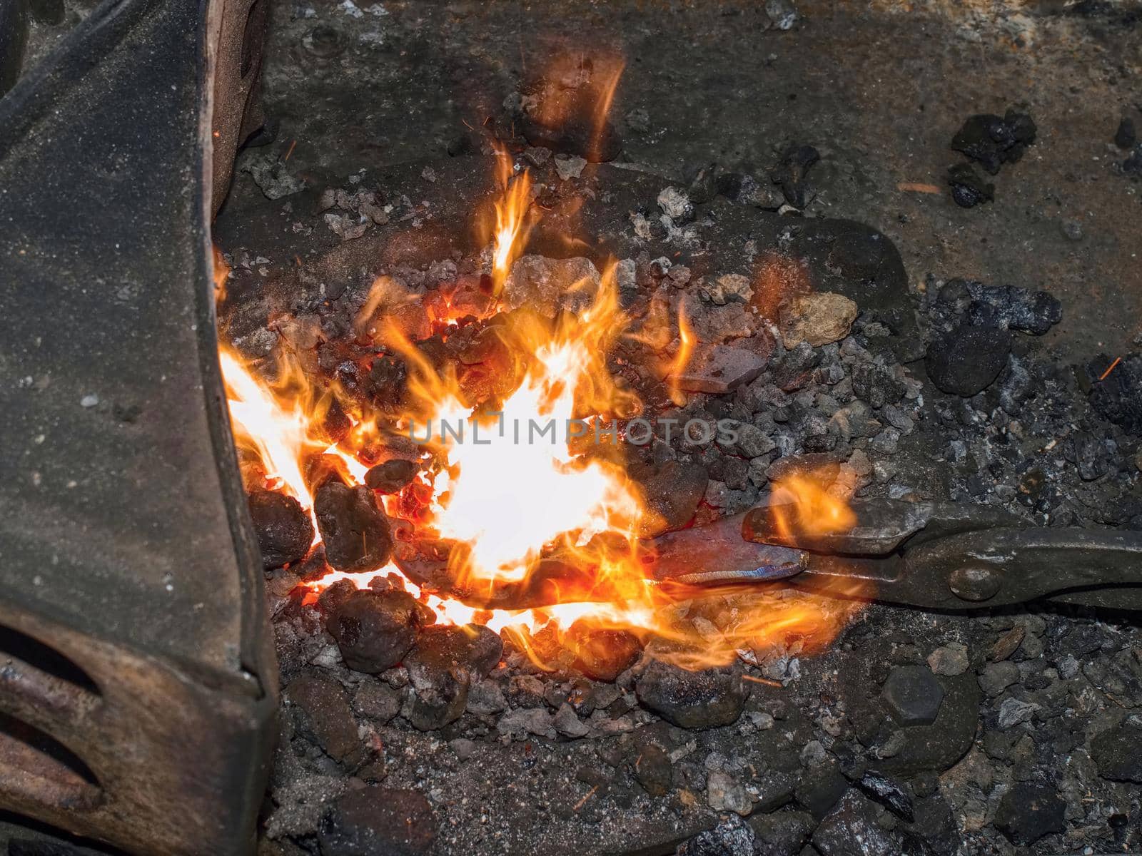 Detail of blacksmith  forge with strong flames. Long pliers hold the hot horse shoe.