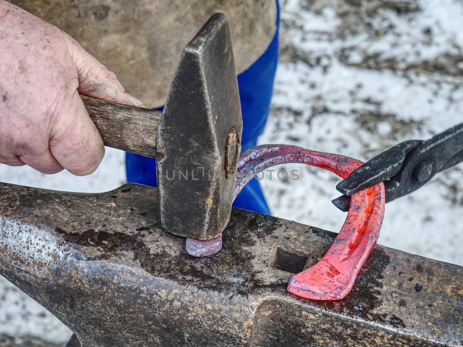 Blacksmith working hard to finalize horseshoe. Smithy process on the anvil. Hammering of glowing steel.