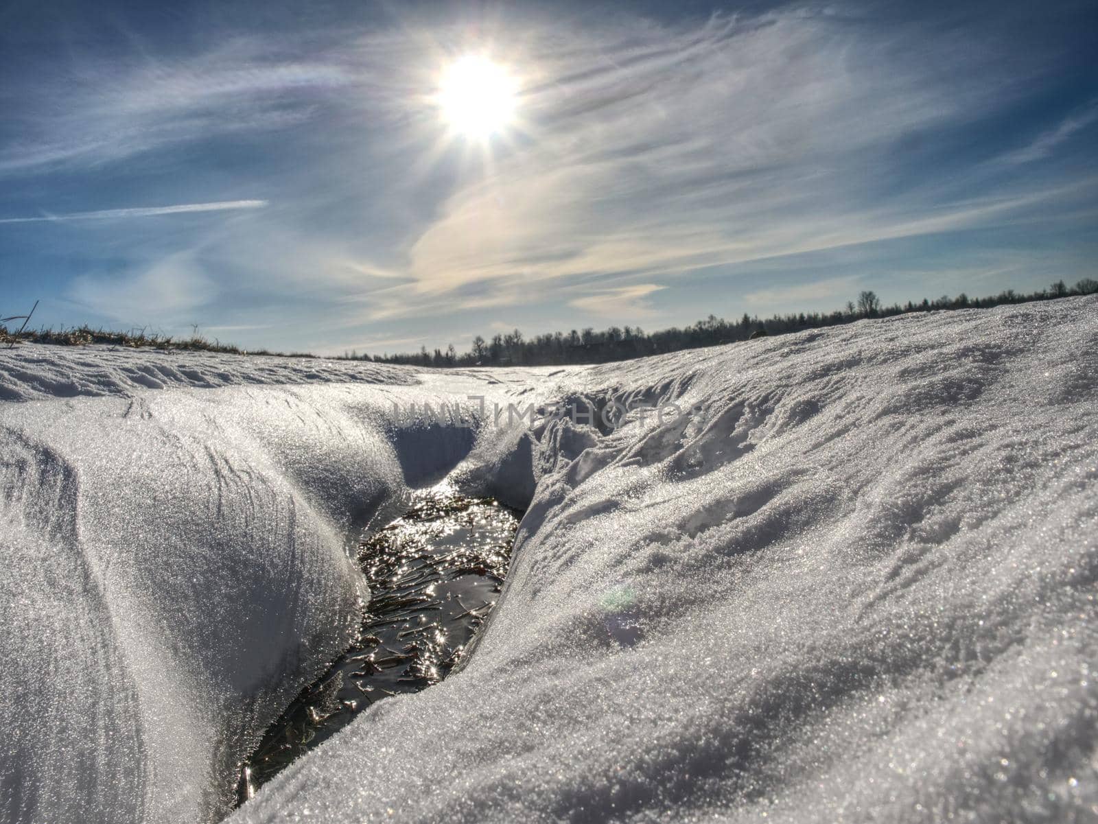 Hole in icy snow with sun flares. Lovely winter scene.