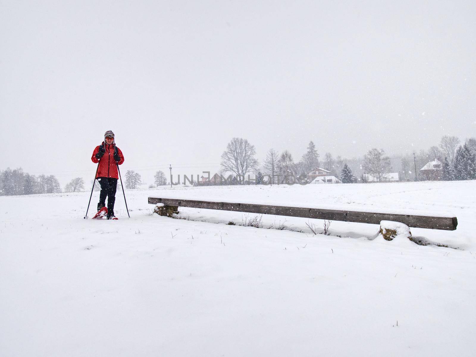 Winter snowshoing in fresh snow. Woman walk whiel snow falling from heavy grey clouds, windy cold weather.