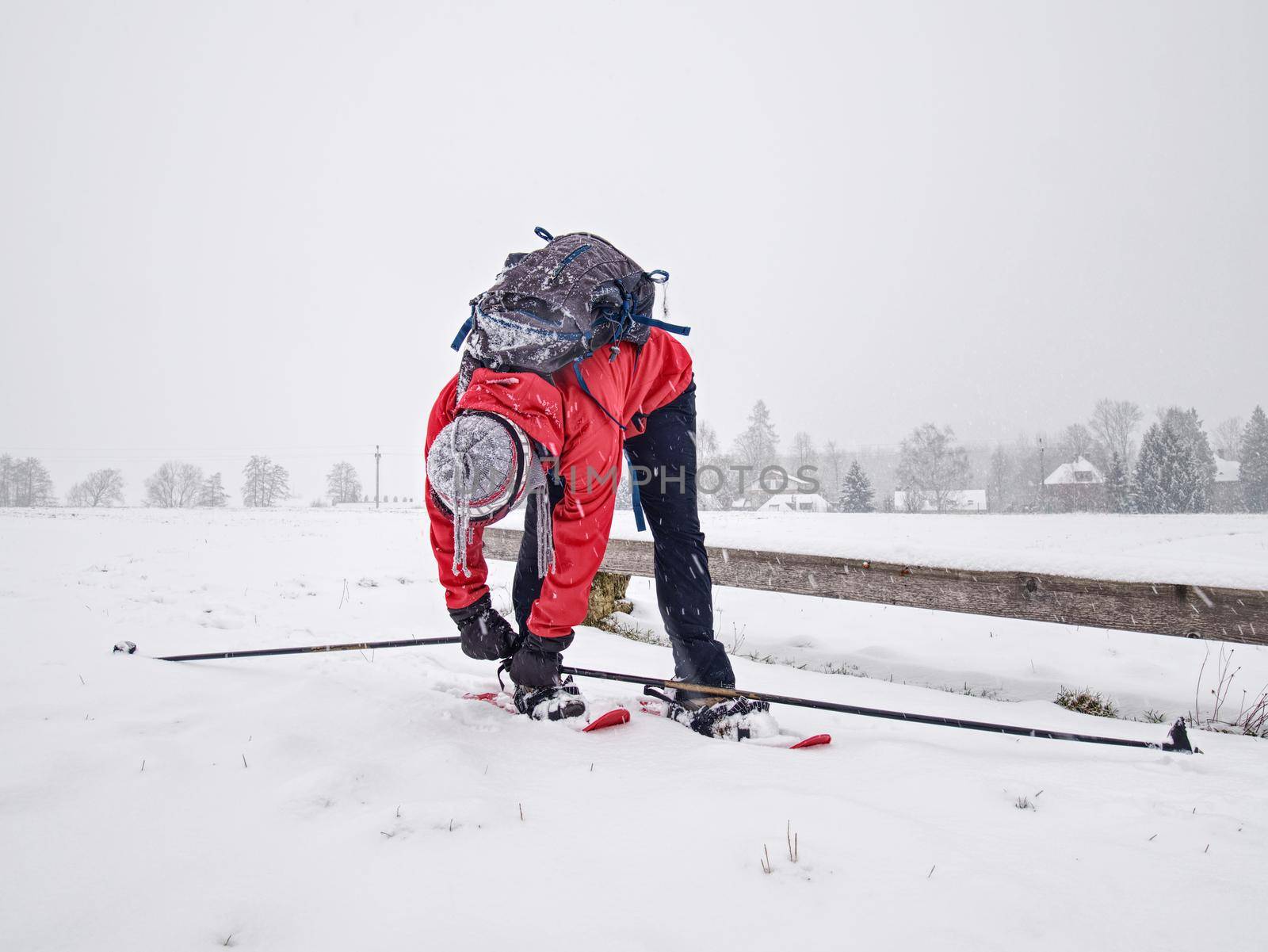 Winter snowshoing in fresh snow. Woman walk whiel snow falling from heavy grey clouds, windy cold weather.