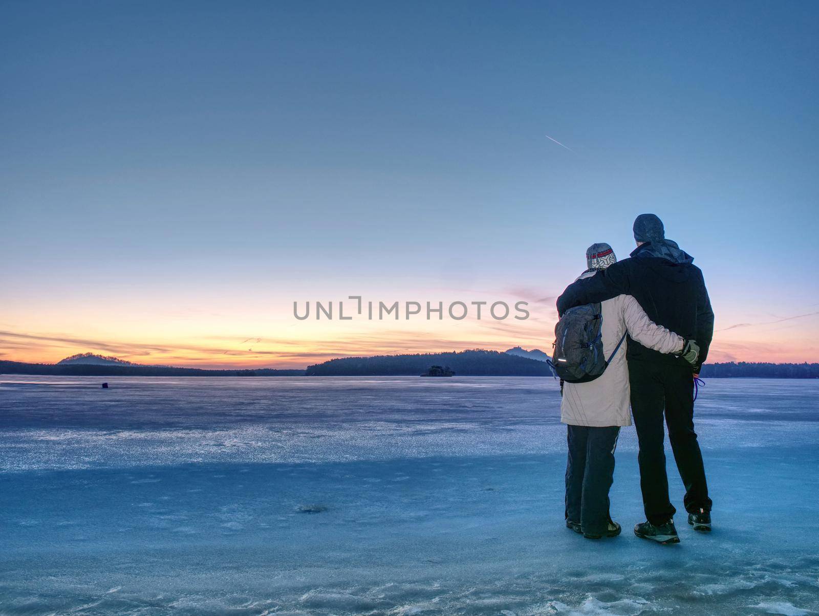 Couple holding by hands. Beautiful young couple in puffy jackets holding hands and enjoying winter daybreak, hiking at frozen pond or lake