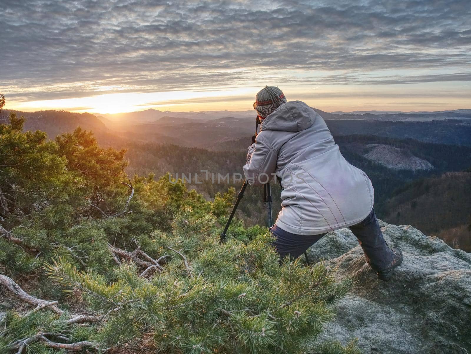 Hiker and photo enthusiast stay with tripod on cliff. Peak with woman taking photos in morning sunrise
