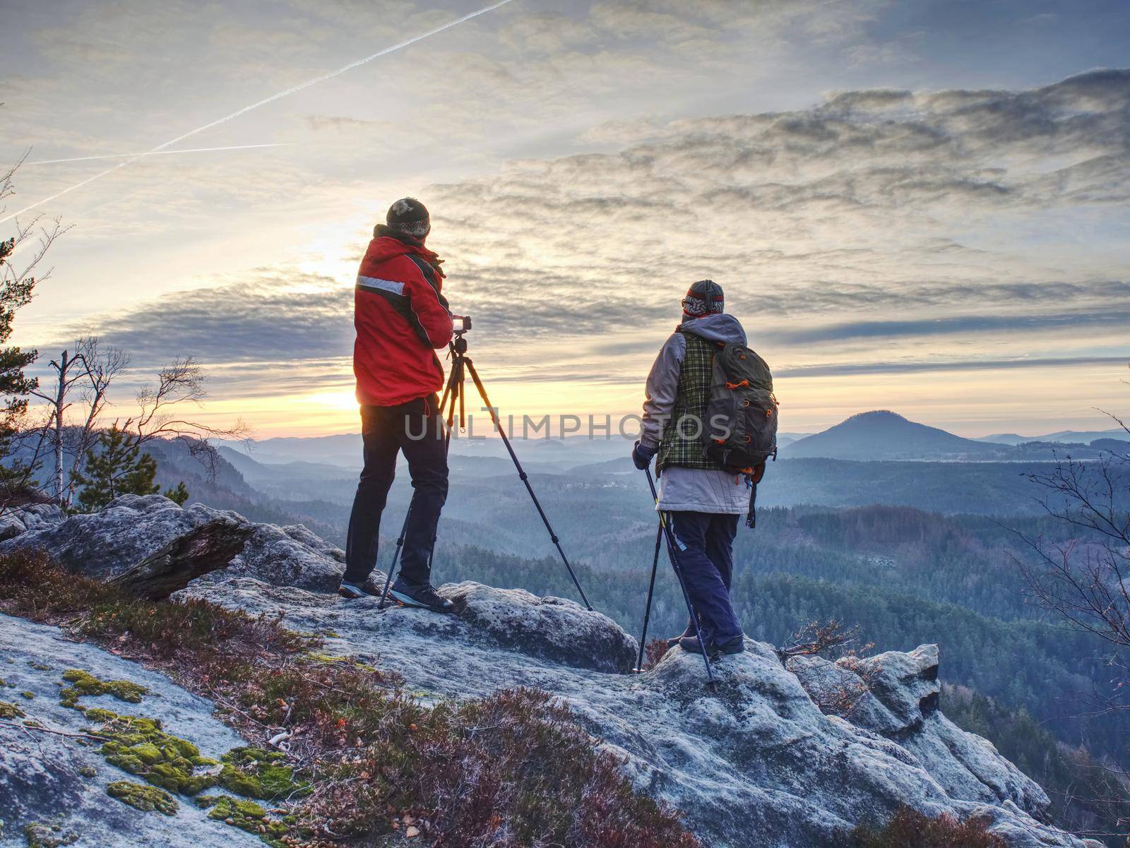 Two photographers with camera and tripod stay along the path in mountains, looking at the hilly horizon