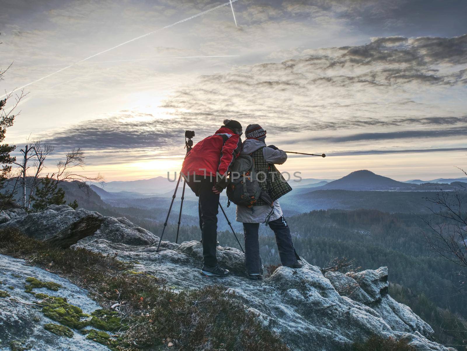 Couple  enjoy photographying in wild nature. Nature photographer with big camera on tripod stay on summit rock. Listen to muse.