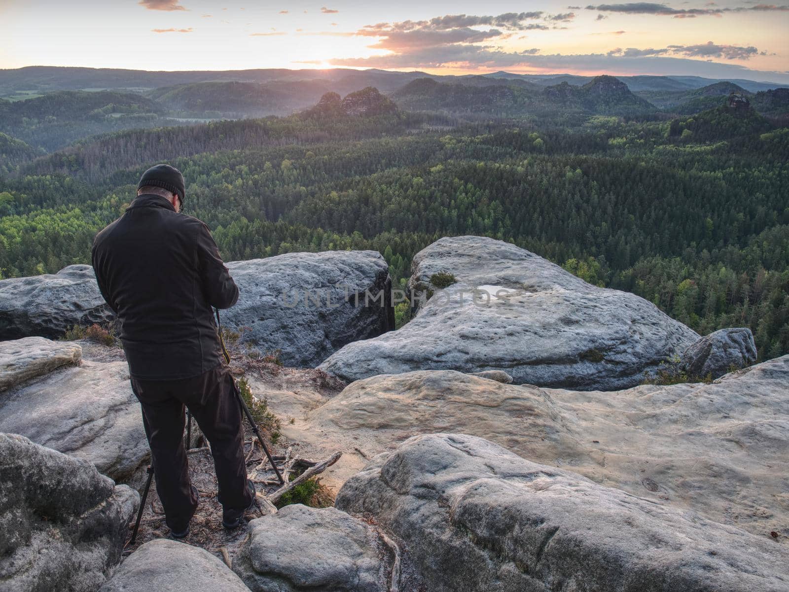 Photographer check display of camera on tripod. Man stay on cliff and takes photos talk friends. Autumn beautiful misty landscape misty sunrise at horizon.