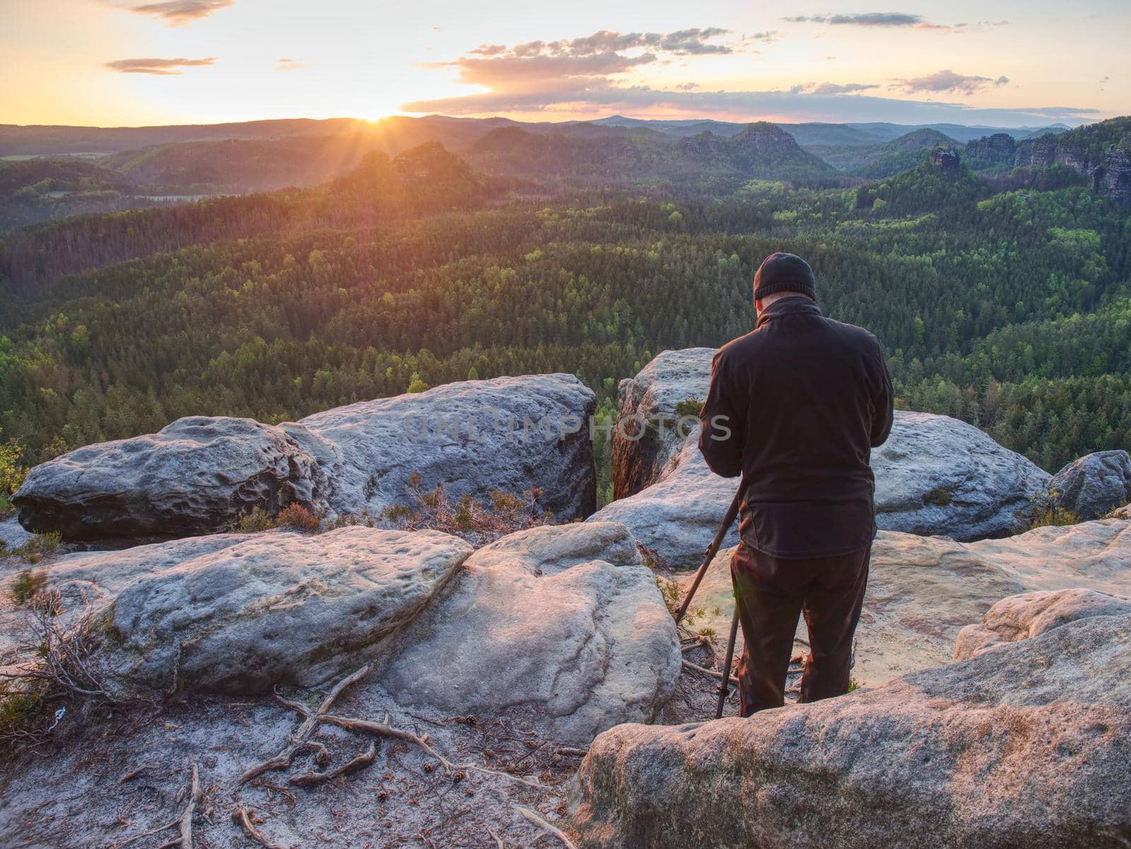 Nature photographer hold tripod with camera. Man at sunrise at open view on mountain peak blue sky