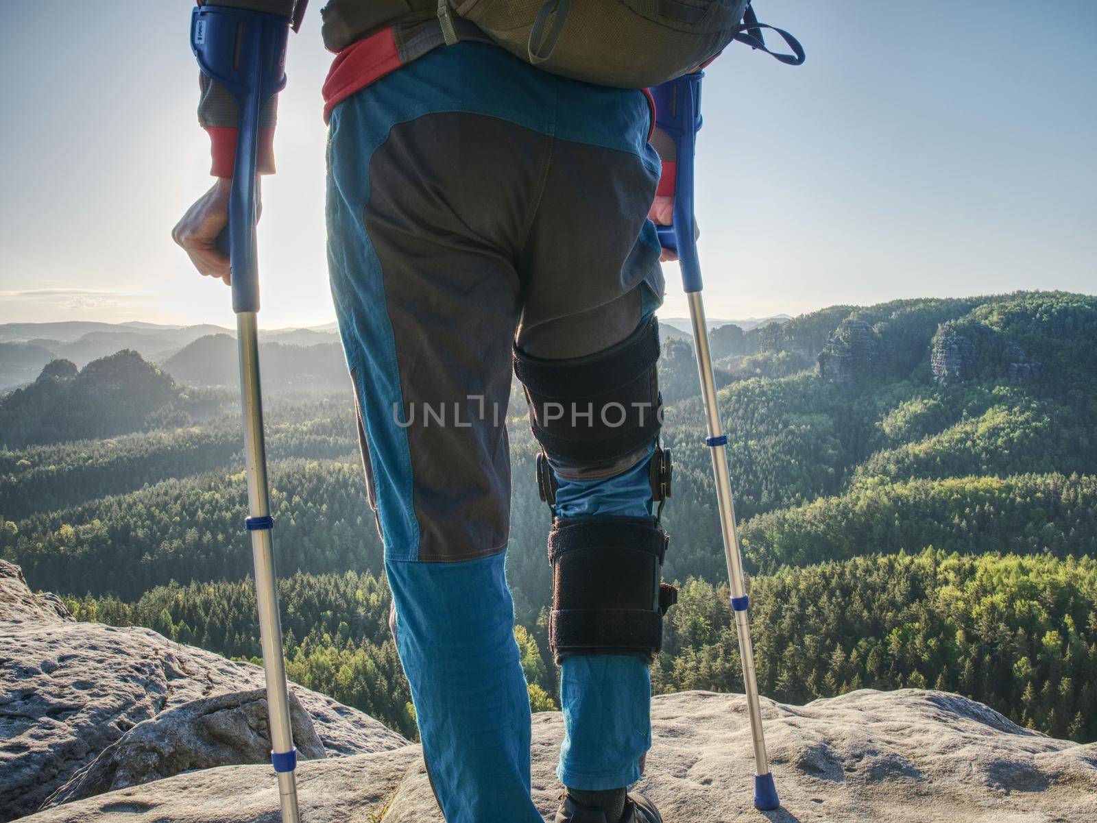 Injured tourist in detail with knee fixed in knee brace feature. Scenic mountain top with deep misty valley bellow