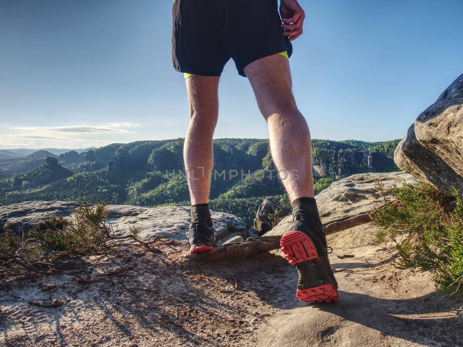 Sportsman on trail. Slim body man in yellow jersey, black shorts and black running shoes run in wild nature.