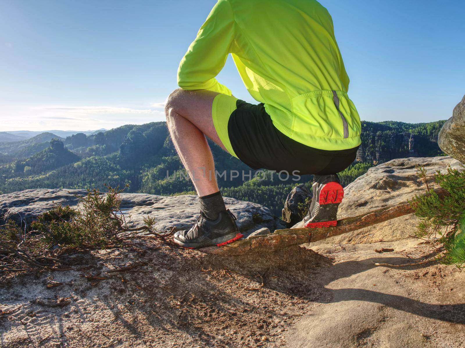 Successful runner man raising body on the cliff with the golden green jersey, sunny blue sky in  background