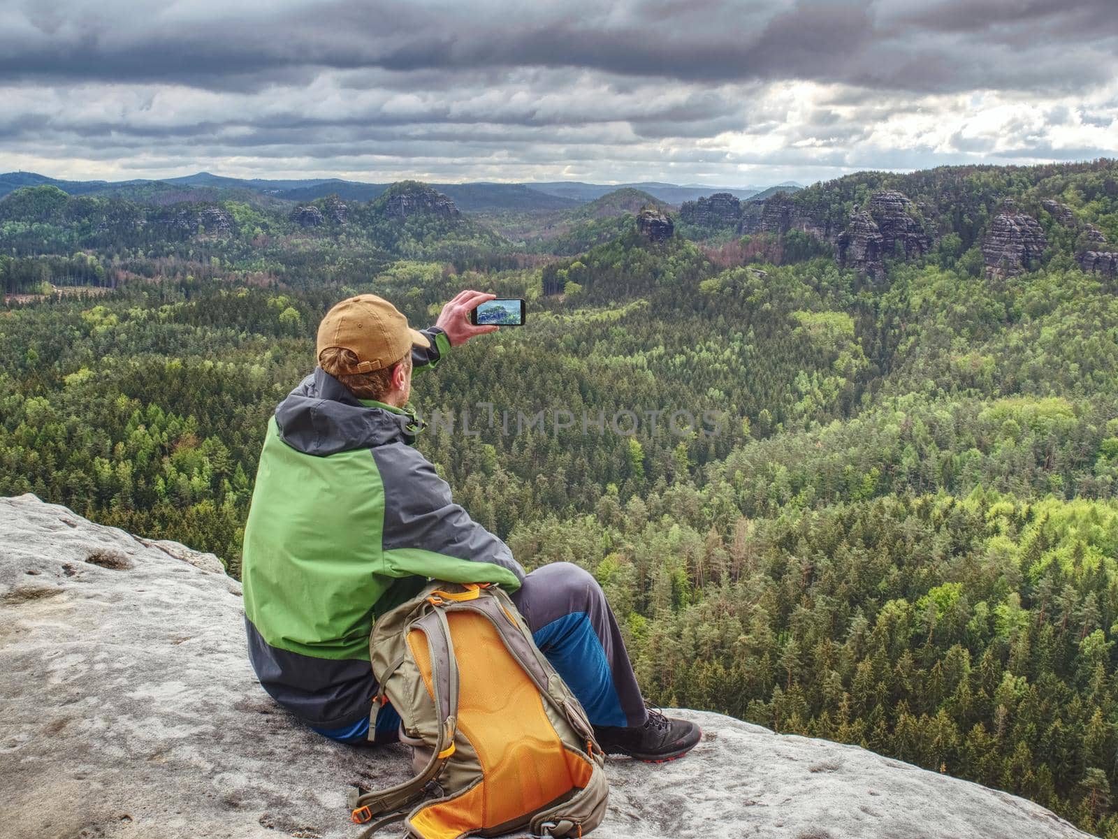 Man tourist in nature. Spring free day in rocky mountains. Hiker with sporty backpack stand on rocky view point above landscape