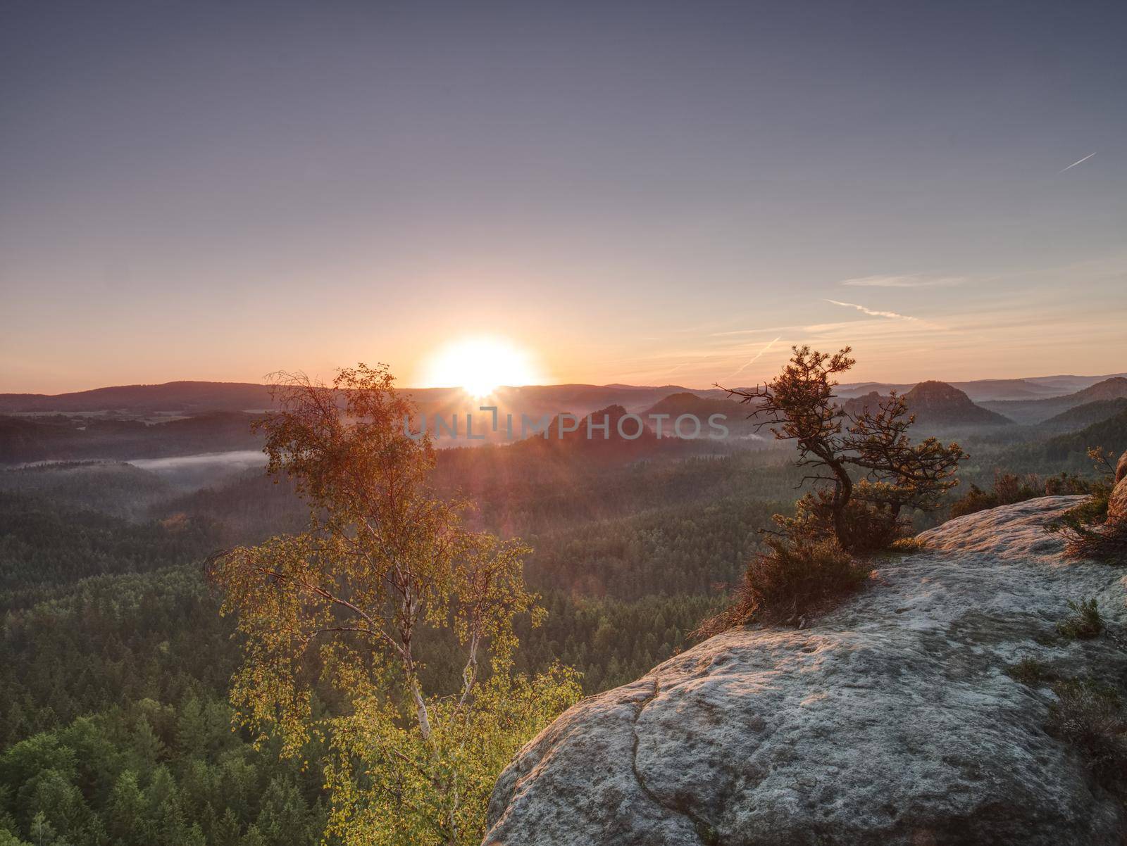 Strong sun rays make long strips in the mist.  Beautiful Landscape with Bright Sunset in the Mountains