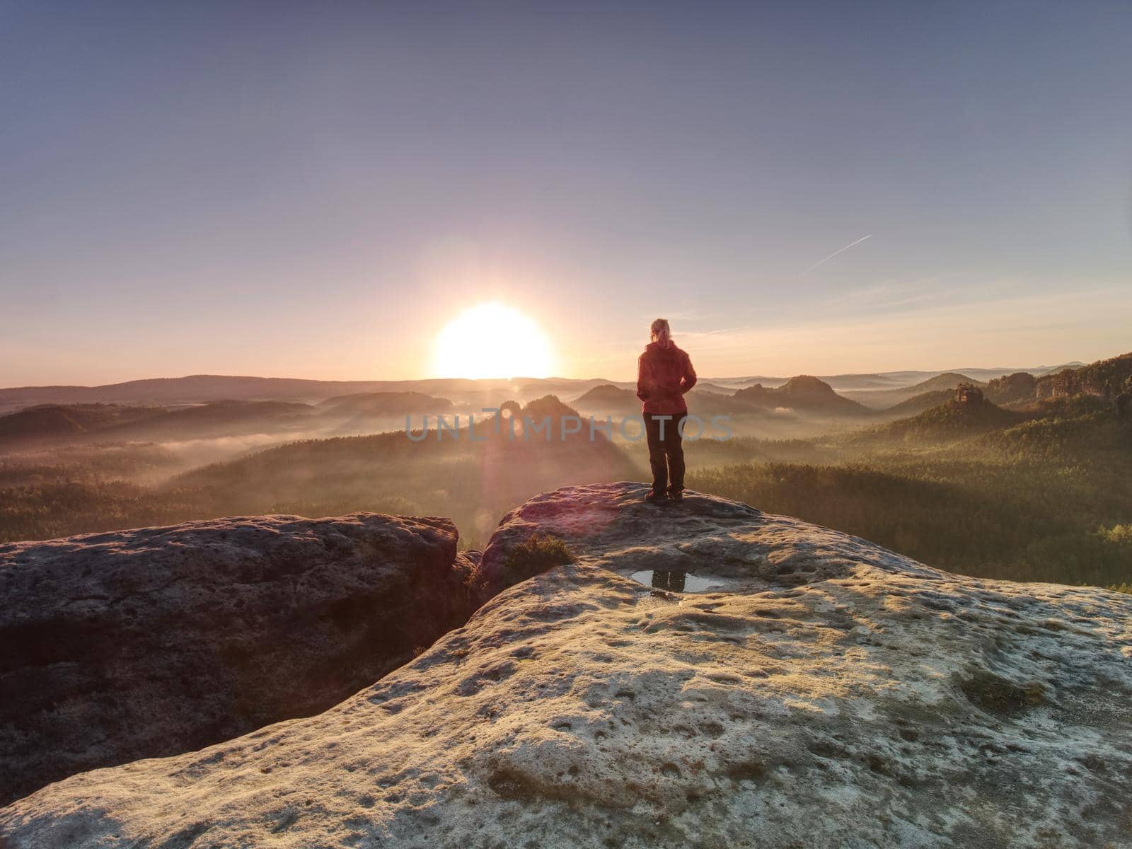 Blong hair woman in sun rays bath and flares. Girl on rocky view point at the end of the world