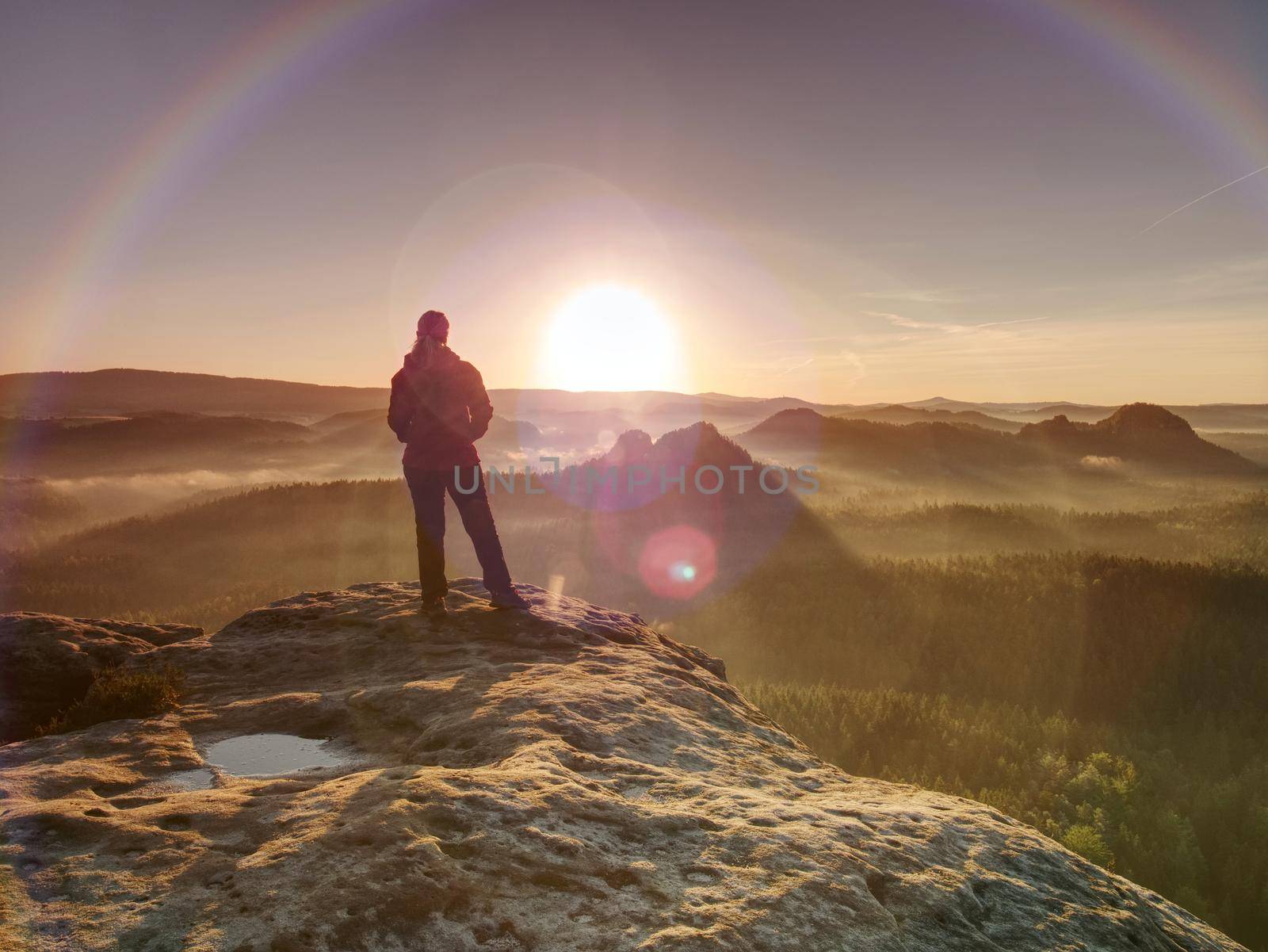 Women in morning Sun. Hiker girl stay in strong Sun rays with many flares around her body. Morning misty nature in background