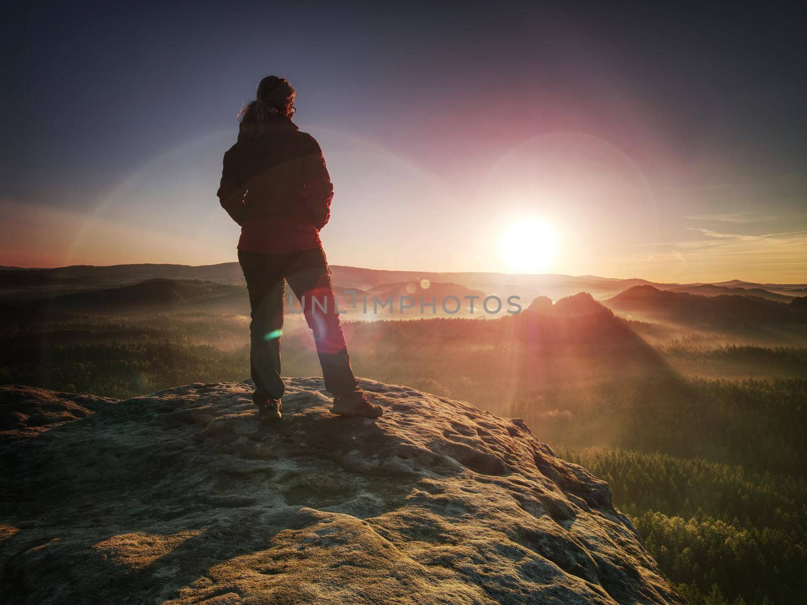 Women in morning Sun. Hiker girl stay in strong Sun rays with many flares around her body. Morning misty nature in background