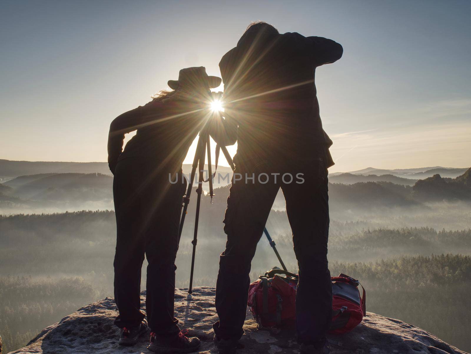 Two hikers taking pictures and talk on top of the mountain. Hikers photographers with photo gear relaxing on top of a mountain and enjoying the view of valley
