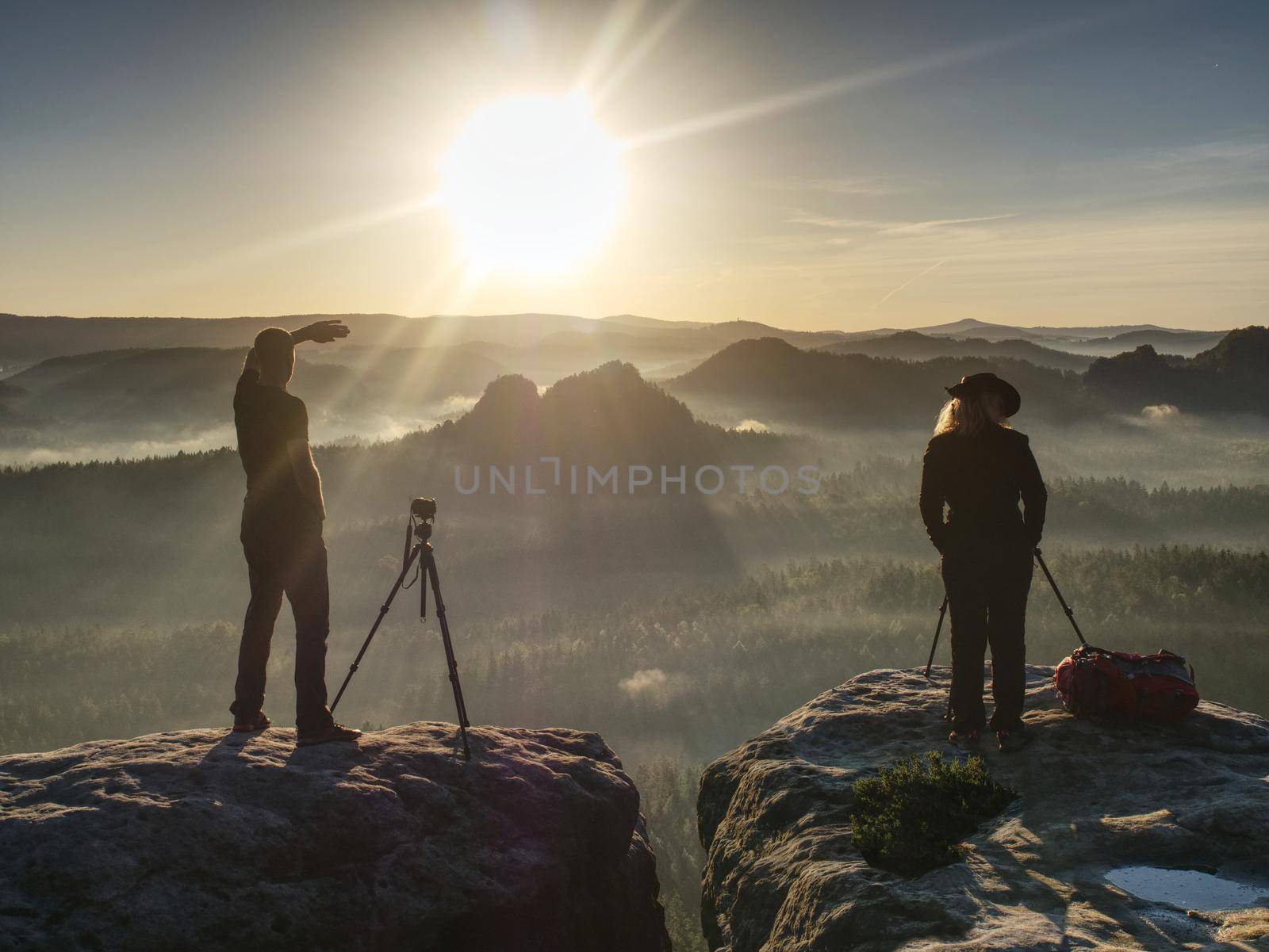 Two hikers taking pictures and talk on top of the mountain. Hikers photographers with photo gear relaxing on top of a mountain and enjoying the view of valley