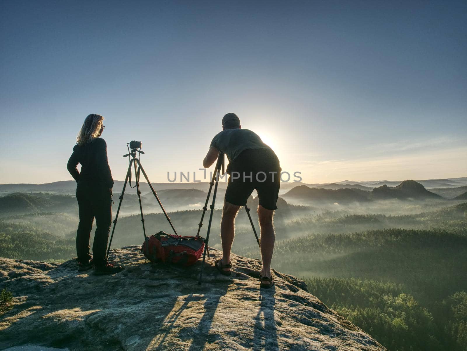 Creative artists stay at own cameras on tripods.  Hikers and photo enthusiasts work together on cliff and thinking