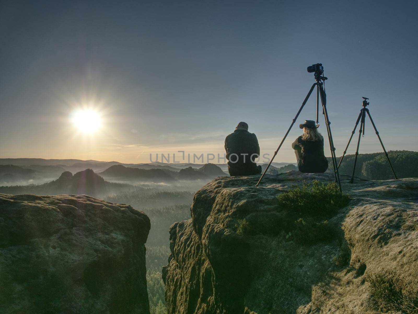 Couple tourists with tripods and cameras take pictures to the background of beautiful hills and sky. Young people in a mountain hike. Freedom and travel concept.